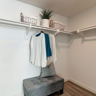 A neatly organized closet with a small bench, clothes hanging on a rod, and decorative baskets on shelves.