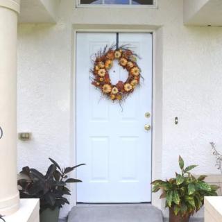 A front door decorated with a sunflower wreath, flanked by potted plants.