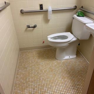 A clean and accessible bathroom featuring a toilet, grab bars, and tiled flooring.