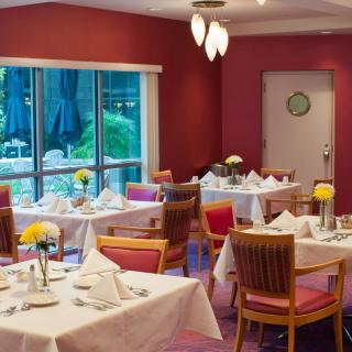 A well-arranged restaurant dining room with neatly set tables and chairs, featuring large windows providing a view of the outside.