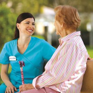 A nurse and an elderly person having a friendly conversation outdoors.
