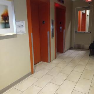 A view of a hallway featuring orange elevator doors, tiled flooring, and a piece of artwork on the wall.