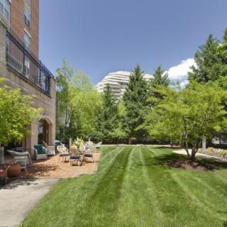 A well-maintained garden with green lawn and trees, bordered by a building and outdoor seating.