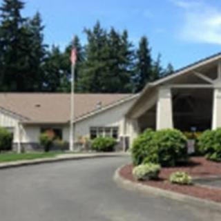 A building with a driveway and landscaping, surrounded by trees.