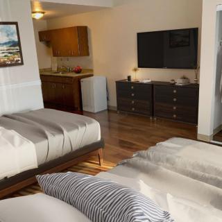A modern hotel room with two beds, a TV, and a kitchenette area.