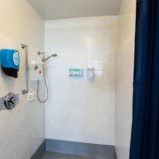 A spacious shower area with a curtain, featuring a wall-mounted showerhead and soap dispensers.