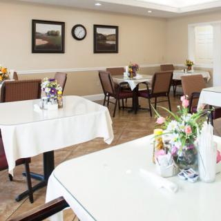 A clean and neatly arranged dining room with tables set for guests, featuring floral centerpieces.