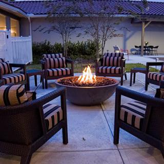 A cozy outdoor patio area with a central fire pit surrounded by cushioned chairs at nighttime.