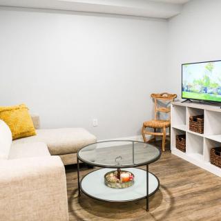 A minimalist living room with a cozy sofa, round glass coffee table, and a television on a shelf unit.