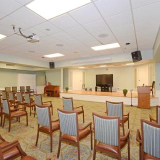 A spacious conference room with a seating arrangement facing a stage equipped with a podium and a large TV screen.