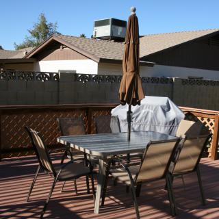 A patio with a table, chairs, umbrella, and grill on a sunny day.