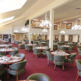 A spacious dining area with multiple tables and green chairs, adorned with elegant chandeliers.