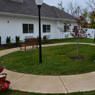 A peaceful garden area with a circular sidewalk, bench, and lamp post in front of a building.