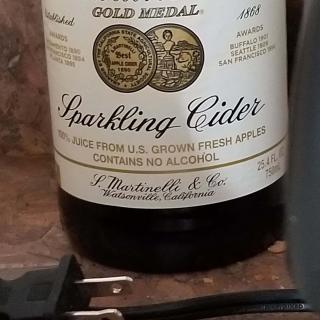 A bottle of sparkling cider next to an electrical plug in a kitchen setting.