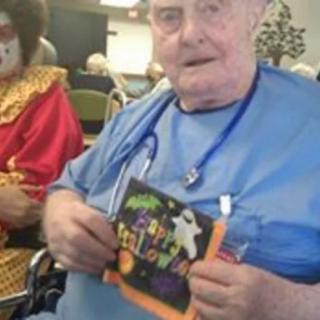 An elderly person holding a Halloween card next to a person dressed as a clown.