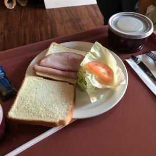 A simple breakfast plate featuring bread, ham, and fresh vegetables.