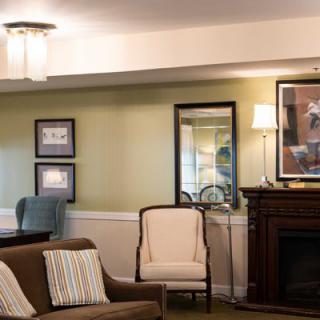 A cozy living room with a sofa, armchair, and fireplace complemented by wall art and a mirror.