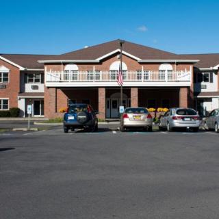 A two-story brick building with a parking lot and several cars in front, under a clear blue sky.