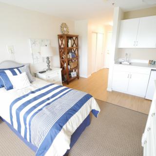 A cozy bedroom with a single bed featuring striped bedding, a shelf, and minimalist decor.