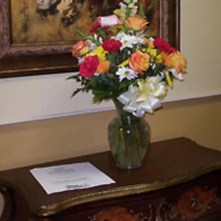 A colorful bouquet of flowers in a vase placed on a decorative table beside a framed artwork.