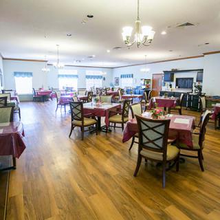 A spacious dining area with multiple tables and chairs, featuring a chandelier and wooden flooring.