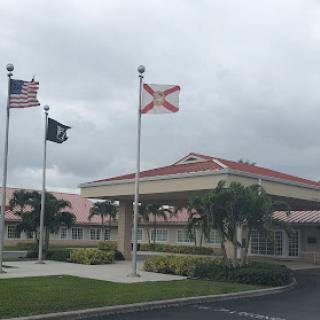 Entrance of a building featuring the American and Florida state flags on a cloudy day.