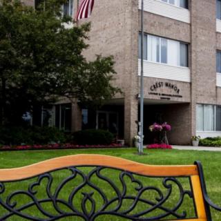 An outdoor bench in front of a multi-story brick building, with a well-kept lawn and an American flag displayed.