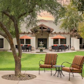 A serene outdoor seating area surrounded by lush greenery and a charming building in the background.