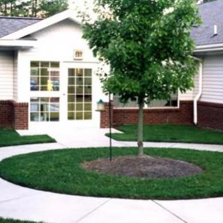A house with a well-maintained lawn and a tree in the front yard, featuring a curved pathway.