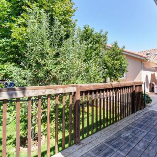 A wooden deck with railing overlooking a lush backyard on a sunny day.