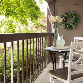 A cozy balcony with a small table and chairs, adorned with plants and a decorative wreath.