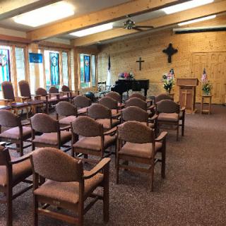 A serene interior of a chapel featuring rows of chairs, a piano, and beautiful stained glass windows.