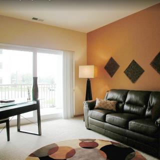 A modern living room with a black leather sofa, geometric wall decor, and a large window letting in natural light.