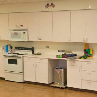A modern kitchen with white cabinets, a stove, microwave, and a trash bin.