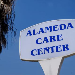 A sign for Alameda Care Center against a clear blue sky.