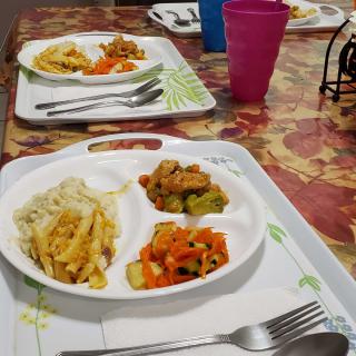 A dining table set with trays of food including vegetables and pasta.