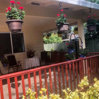 A cozy patio with hanging flower pots, outdoor seating, and a wooden fence.