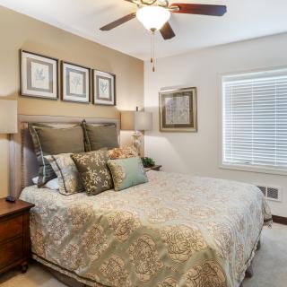 A cozy and well-furnished bedroom with a large bed, decorative pillows, wall art, and a ceiling fan.