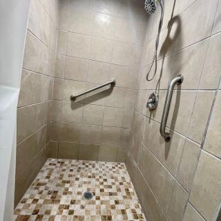 A modern shower with tiled walls and a mosaic floor, featuring stainless steel grab bars and a handheld showerhead.