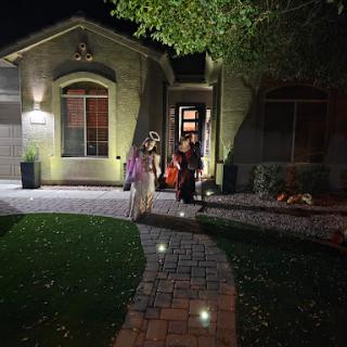 Children walking towards a well-lit house on a pleasant night.