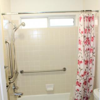 A bathroom with a shower featuring a floral curtain and safety grab bars.