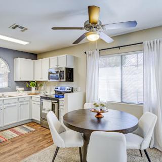 A bright and modern kitchen with a cozy dining area, featuring white cabinetry and a ceiling fan.