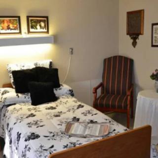 A cozy bedroom with a single bed and floral bedding, accompanied by an armchair and wall decorations.