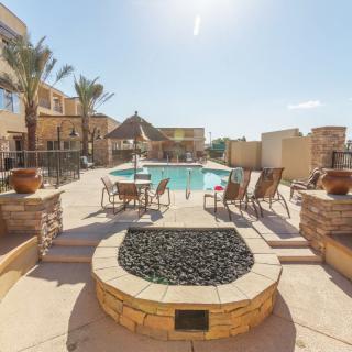 A sunny outdoor pool area with lounge chairs and a fire pit surrounded by palm trees.