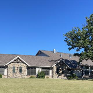 A stone facade house with a large lawn and a tree under a clear blue sky.