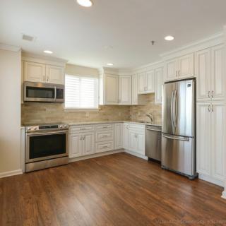 A modern kitchen featuring white cabinets, hardwood flooring, and stainless steel appliances.