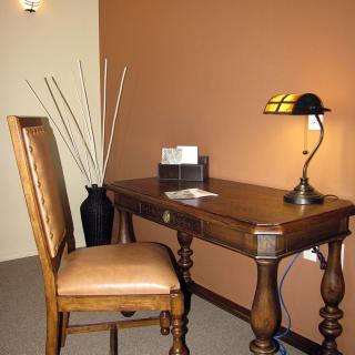 A cozy workspace featuring a wooden desk and chair, completed with a decorative lamp and vase.