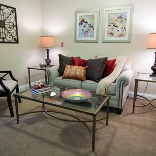 A cozy living room with a sofa and decorative pillows, flanked by side tables and lamps, featuring artwork on the walls.