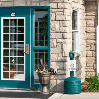 A building entrance featuring a glass door with a stone wall and a planter nearby.