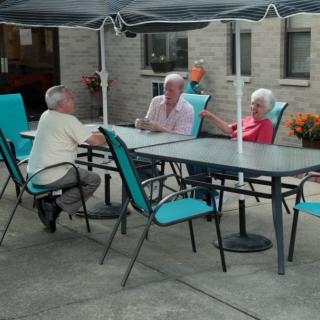 A group of people sitting and conversing at an outdoor patio table under a canopy.